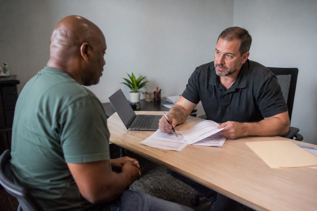 Veteran getting VA benefits claim assistance at home desk with paperwork and laptop in 2026